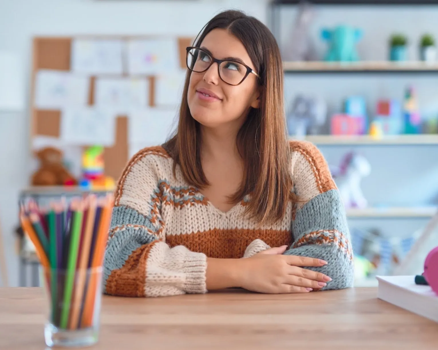 An educator sitting at her desk looks up thoughtfully with a slight smile on her face.