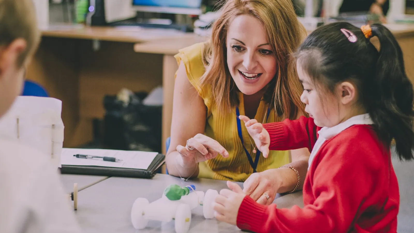 Teacher at desk helping young student.