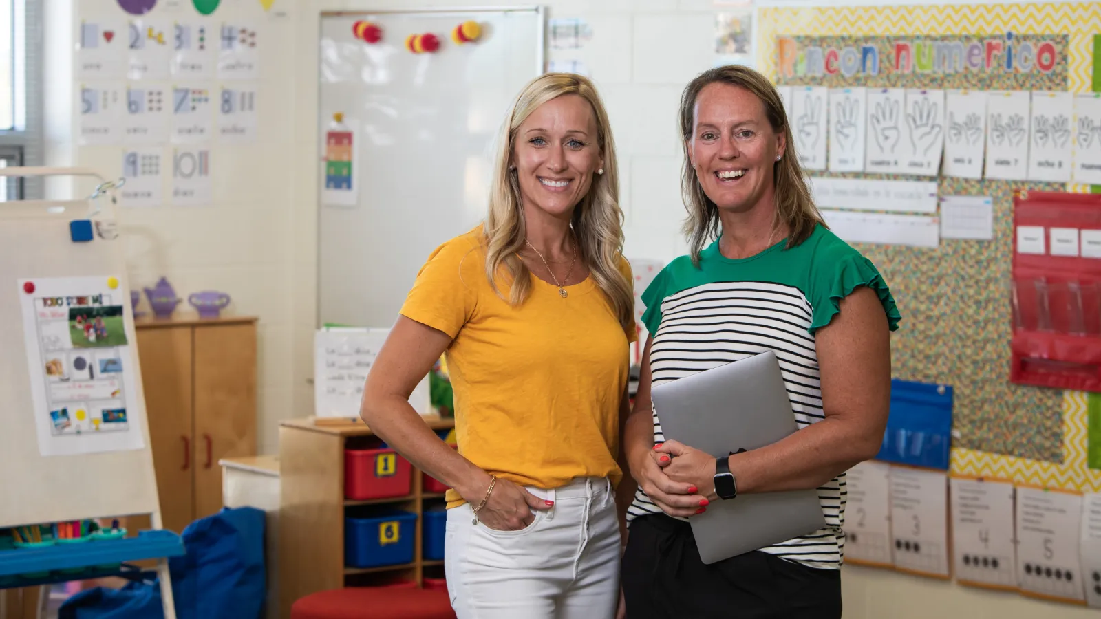Two teachers standing in classrom smliing for the camera