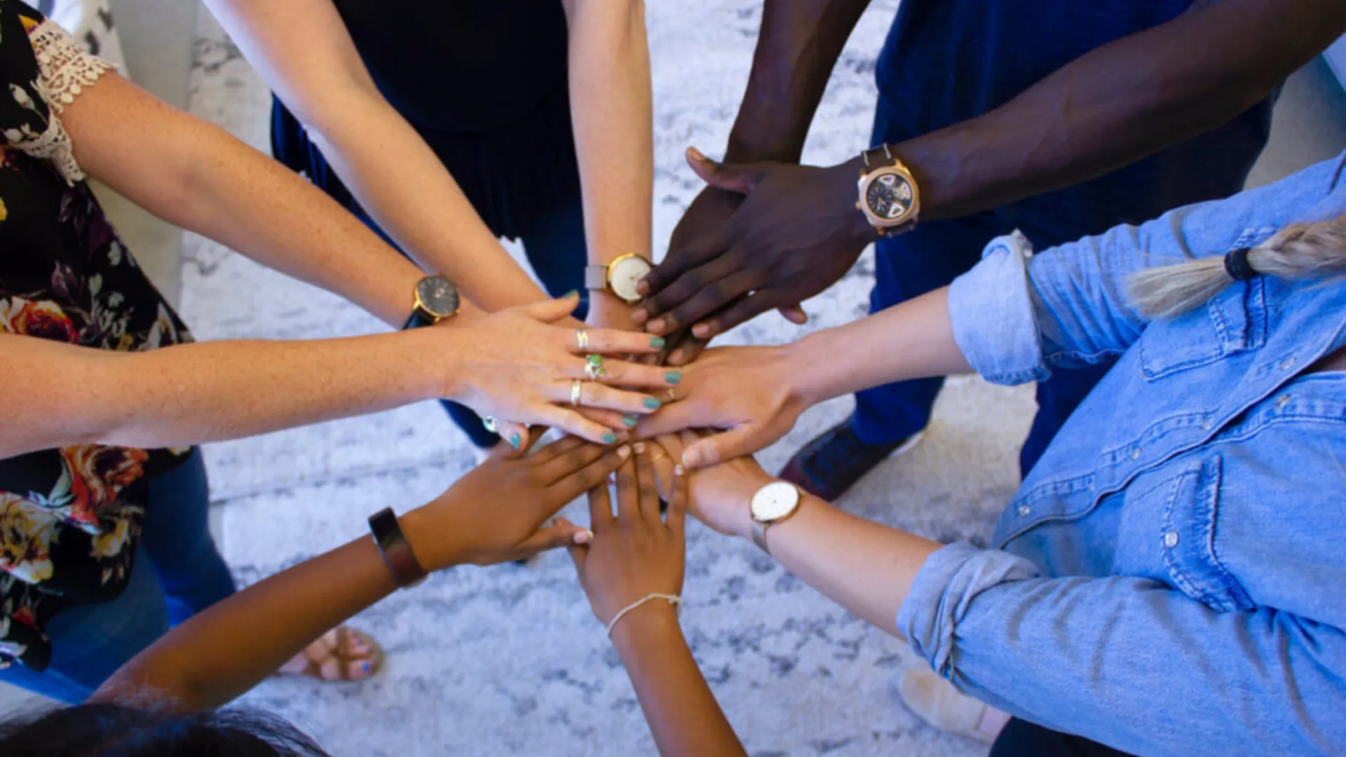 Group in a circle reaching hands together of all different skin tones