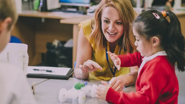 Teacher at desk helping young student.
