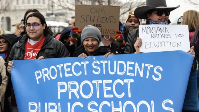 NEA Members at a rally holding blue Protect Students Protect Public Schools sign
